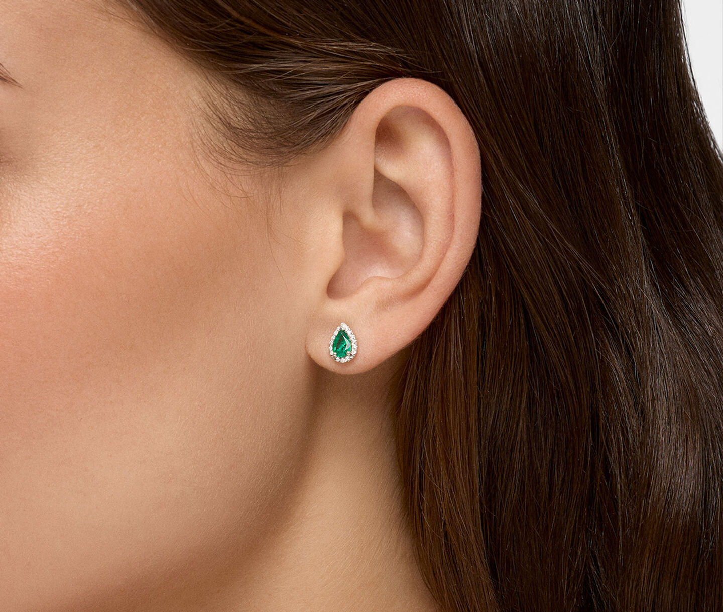 A woman wearing Birks Essentials emerald and diamond stud earrings.